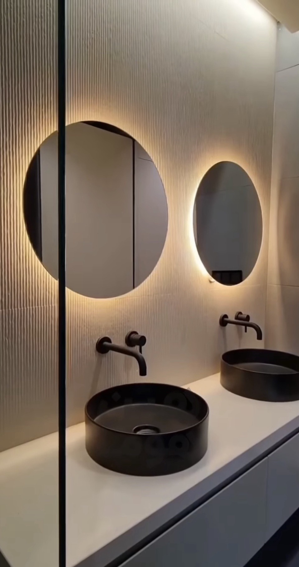 Bathroom vanity with double black vessel sinks and backlit round mirrors